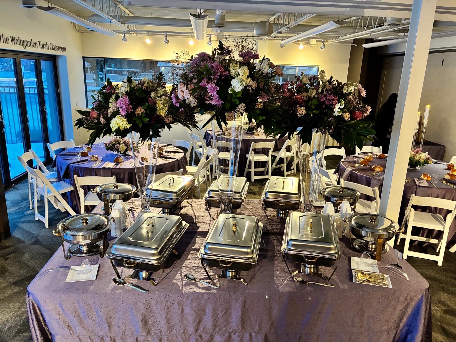 Buffet setup with chafing dishes and tall purple florals at the Weingarden Torah Classroom